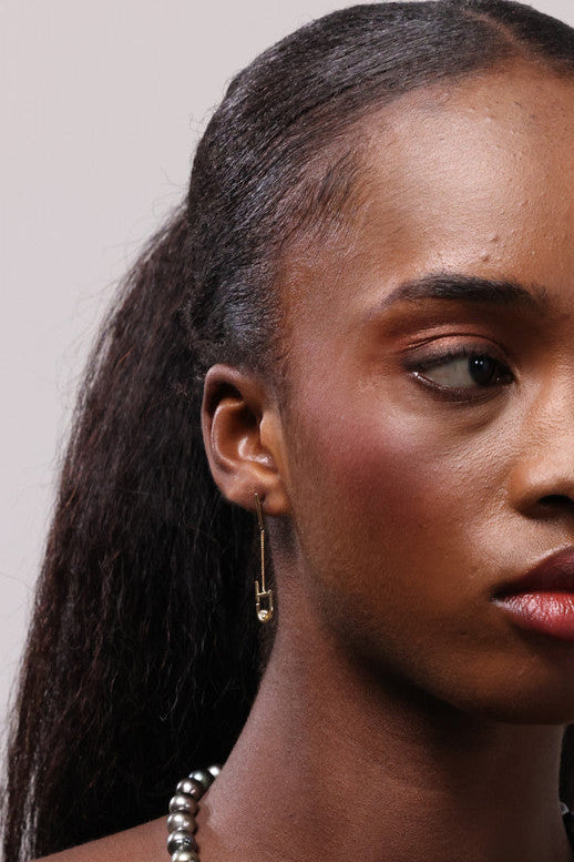 Woman wearing a dark brown top, pearl necklace and gold earrings