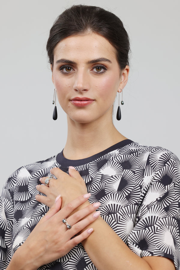 Woman wearing a black and white patterned top with earrings and rings on a gray background